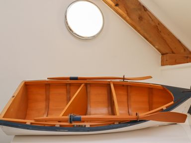 A wooden rowboat with paddles indoors under a wooden ceiling beam at The Boathouse (Seahouses) in Seahouses
