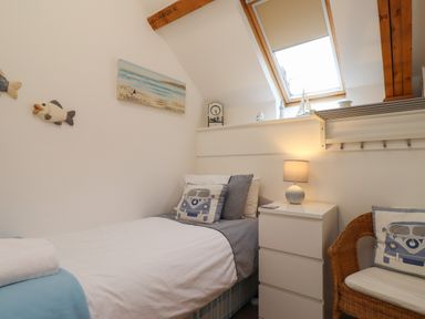 A small bedroom with a single bed a white bedside cabinet with a lamp a wicker chair and a skylight window at The Boathouse in Seahouses