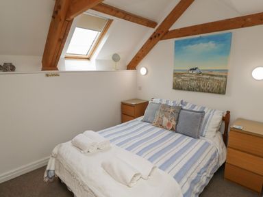 A bedroom with a bed with striped bedding two wooden dressers and a skylight window at The Boathouse in Seahouses