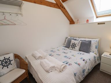 A bedroom with a bed made with patterned bedding and rolled towels a wicker chair with a cushion and a skylight at The Boathouse (Seahouses) in Seahouses