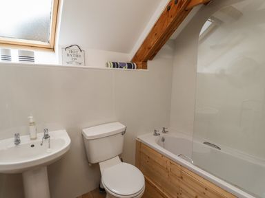 A bathroom with a toilet sink and bathtub under a slanted ceiling with a window at The Boathouse (Seahouses) in Seahouses
