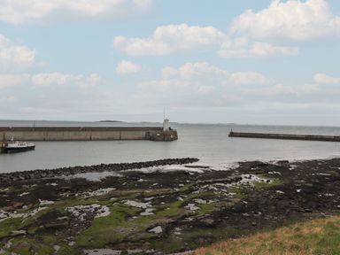 A coastal area with a harbor wall boat and rocky shoreline at The Boathouse (Seahouses) in Seahouses