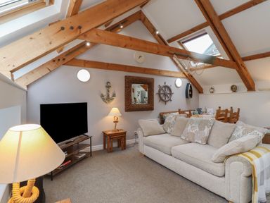 A living room with a beige sofa wooden beams a television and nautical decorations at The Boathouse (Seahouses) in Seahouses