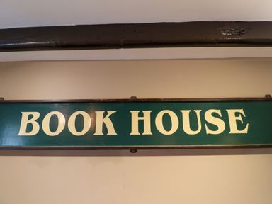 A green sign with white letters that reads Book House on a beige wall at The Book House in Warkworth