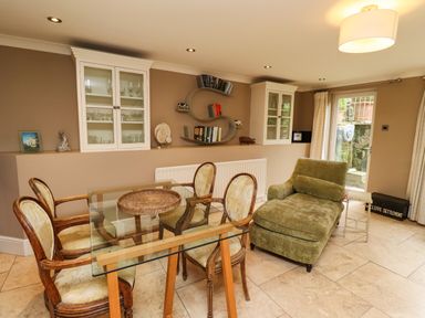 A dining area with a glass table and chairs next to a green chaise lounge in a room with display cabinets at The Book House in Warkworth