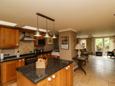 A kitchen with wooden cabinets and a black countertop island with a wooden crate and pendant lights over the island at The Book House in Warkworth