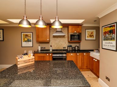 A kitchen with wooden cabinets black granite countertops and three hanging metal pendant lights at The Book House in Warkworth