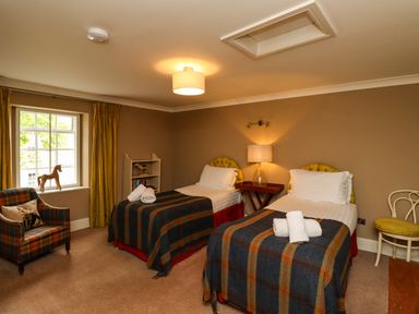 A bedroom with two single beds a chair a small bookshelf and a window at The Book House in Warkworth