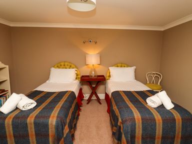 A bedroom with two single beds a bedside table with a lamp and a chair at The Book House in Warkworth