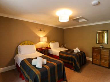 A bedroom with two single beds a lamp on a bedside table a wooden chair a chest of drawers with a mirror above at The Book House in Warkworth