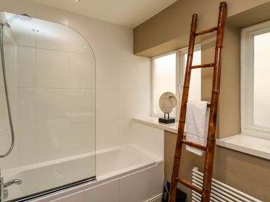 A bathroom with a bathtub shower combination bamboo towel ladder and two frosted windows at The Book House in Warkworth