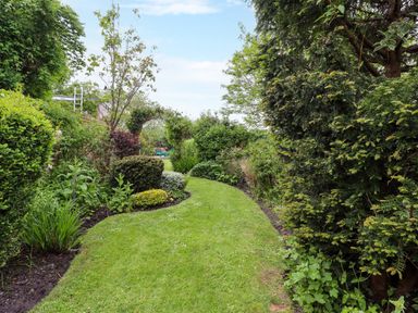 A garden with a curved grass path surrounded by bushes and plants at The Book House in Warkworth