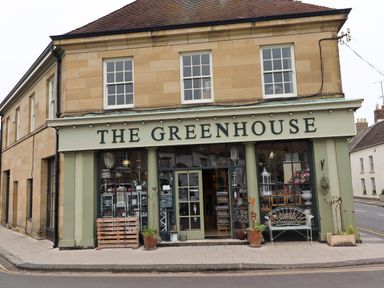 A shop front named The Greenhouse with large windows and potted plants outside