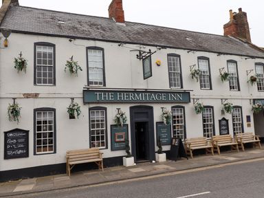 Exterior of The Hermitage Inn with multiple windows benches and hanging flower baskets at The Hermitage Inn in Warkworth