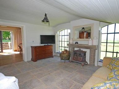 A living room with a dresser mounted TV a fireplace and large arched windows at The Huffy House in Alnmouth