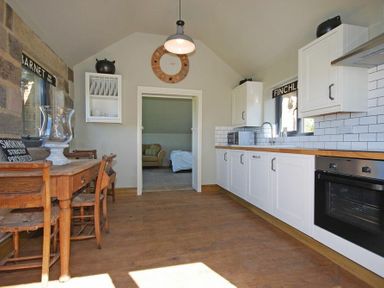 A kitchen with white cabinets wood countertop wooden dining table and chairs and a clock on the wall at The Huffy House in Alnmouth