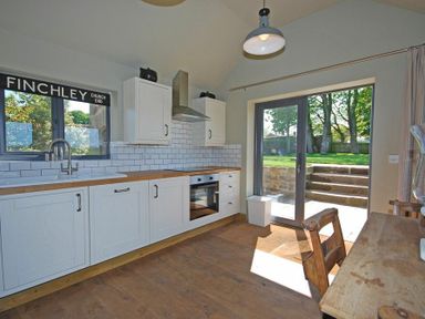 A kitchen with white cabinets wooden countertops and glass doors leading outside at The Huffy House in Alnmouth