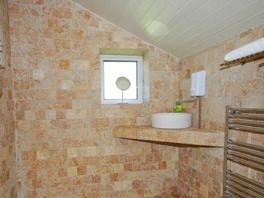 A bathroom with tiled walls a small window a round sink on a tiled countertop a towel rack and folded towels at The Huffy House in Alnmouth