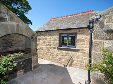 An outdoor stone patio with a built in stone barbecue grill and a stone building with a window at The Huffy House in Alnmouth