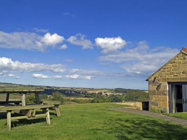 A stone building next to a wooden picnic table on grass with countryside views at The Huffy House in Alnmouth