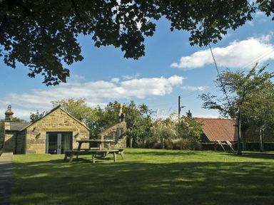 A stone building with a picnic table in a grassy yard with trees and bushes at The Huffy House in Alnmouth