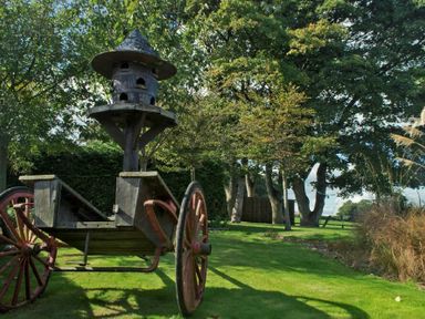A wooden cart with a birdhouse on top on a lawn with trees at The Huffy House in Alnmouth