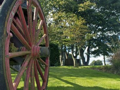 A red wooden wagon wheel on grass with trees in the background at The Huffy House in Alnmouth
