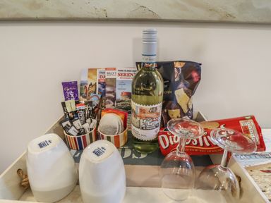 A tray with a bottle of white wine, two inverted glasses, two inverted mugs, packets of tea and coffee, snacks, and brochures at The Little Boathouse in Seahouses