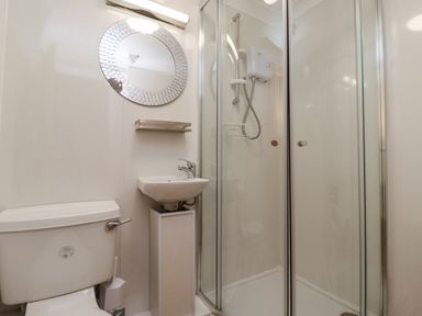 A bathroom with a toilet sink circular mirror and shower enclosure at The Little Boathouse in Seahouses