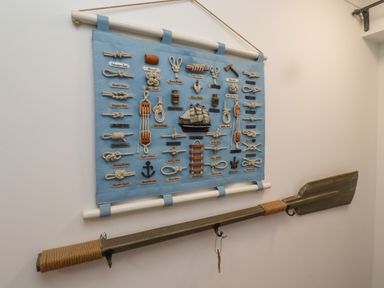 A wall display with various types of knots and a wooden paddle underneath at The Little Boathouse in Seahouses