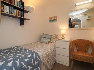 A small bedroom with a single bed next to a white drawer and a wicker chair at The Little Boathouse in Seahouses