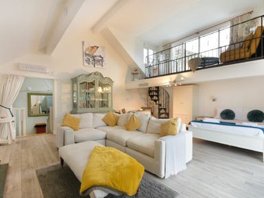 A living room with white sofa yellow cushions a cabinet and a spiral staircase at The Snug in Embleton