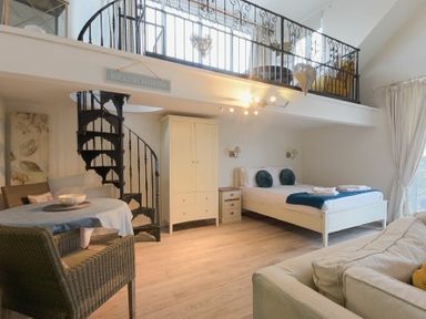 A bedroom with a bed bedside tables wardrobe and a spiral staircase leading to a loft at The Snug in Embleton