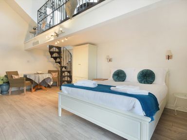 A bedroom with a large bed and blue cushions a spiral staircase table and chairs at The Snug in Embleton