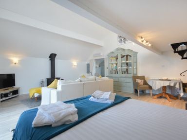 A living area with a bed in the foreground a white sofa a blue cabinet a round table and a television at The Snug in Embleton