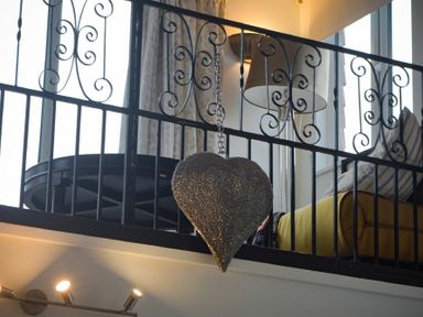 A metal heart ornament hanging from a black wrought iron railing with part of a yellow couch and a lamp behind at The Snug in Embleton