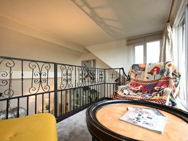 A sitting area with a round wooden table magazines and a colorful blanket over a chair behind a decorative black metal railing at The Snug in Embleton