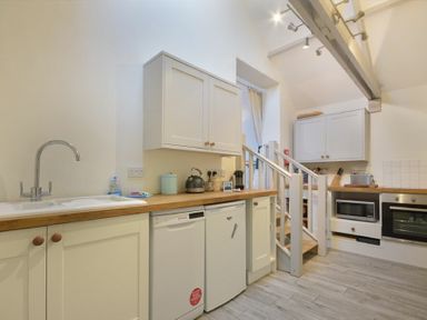 A kitchen with white cabinets wooden countertops a sink dishwasher refrigerator microwave oven and stairs at The Snug in Embleton