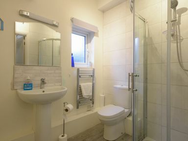 A bathroom with a sink mirror toilet shower and towel rack at The Snug in Embleton