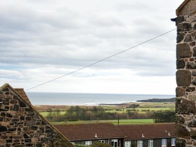 A coastal landscape with houses trees fields and the sea in the background at The Snug in Embleton
