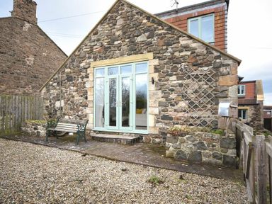 A stone house with light blue double doors a bench mailbox and gravel in the yard at The Snug in Embleton