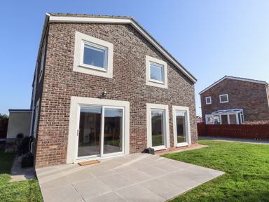 A brick house with white-framed windows and sliding glass door opening to a tiled patio and grass lawn at Tree Corner in Beadnell