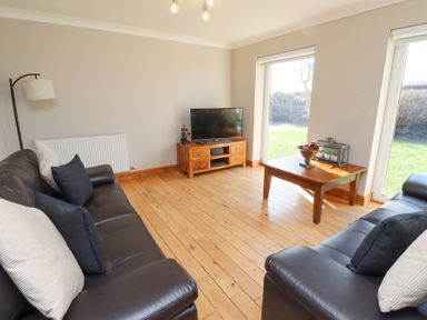 A living room with two black sofas a wooden coffee table and a TV on a wooden stand at Tree Corner in Beadnell