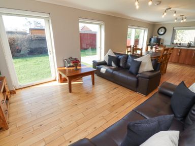 A living room with two dark sofas a wooden coffee table and large windows overlooking a garden at Tree Corner in Beadnell