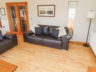 A living room with brown leather sofas and cushions wooden floor and glass double doors at Tree Corner in Beadnell