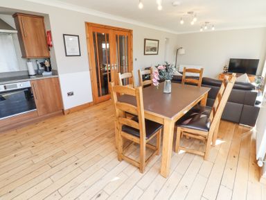 A dining area with wooden table and chairs next to a living room with sofas and a TV at Tree Corner in Beadnell