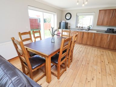 A kitchen with wooden cabinets and a dining table with six wooden chairs and a vase with flowers at Tree Corner in Beadnell