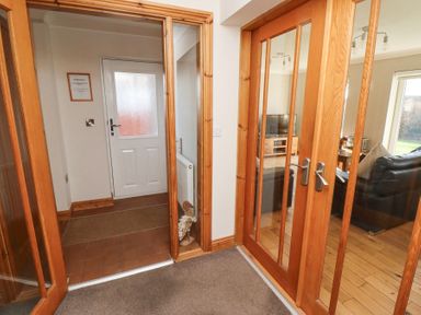 A hallway with wooden framed glass double doors leading to a living room and a white exterior door at Tree Corner in Beadnell