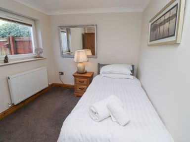 A bedroom with a single bed towel bedside table lamp mirror and window at Tree Corner in Beadnell