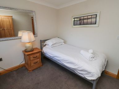 A bedroom with a single bed towels a bedside table with a lamp a large wall mirror and a framed picture at Tree Corner in Beadnell